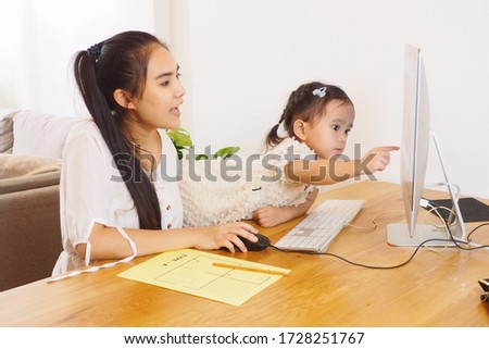 Young beautiful Asian mother teaching her cute daughter using computer and technology for online learning and surfing internet at home. Mother and child activity, lovely family concept     