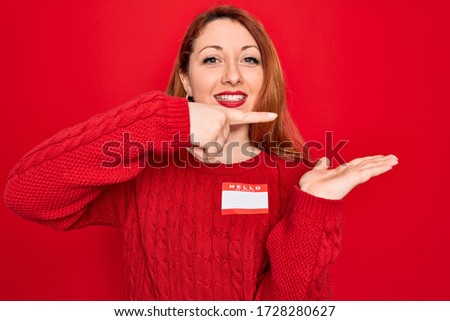 Young beautiful redhead woman wearing sticker presentation with hello my name message amazed and smiling to the camera while presenting with hand and pointing with finger.