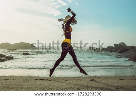 Full length of african woman in bikini running on the beach. Female model on the sea shore enjoying herself.