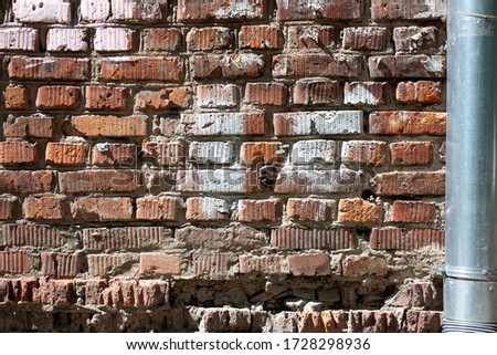 Red brick wall close up. The brick wall is painted red. Remains of an advertisement on a brick wall. A spillway metal pipe is attached to the wall.