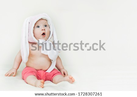 child opened mouth and looks up in surprise. background for sales, shocking news, children's goods. small beautiful baby sitter in rabbit hat.