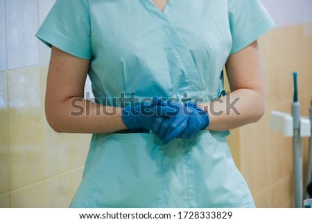 Dentist's office. The dentist's gloved hands are folded and the doctor is standing in a special blue medical uniform. Equipment for dental offices.