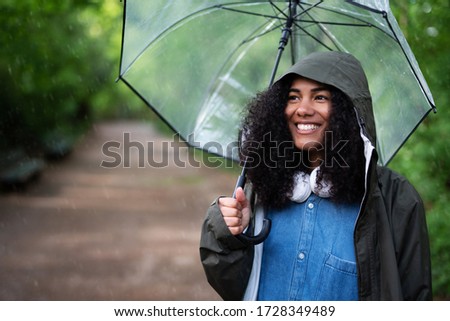 A young woman with rain jacket and umbrella outside in the rain