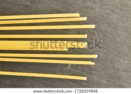 Raw bright yellow spaghetti, close-up, on a slate plate, top view.