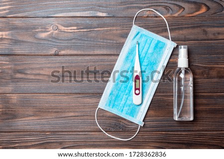 Top view of hygienic surgical mask, digital thermometer and alcohol gel sanitizer on wooden background. Protective equipment concept with copy space.