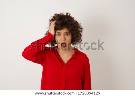 Embarrassed attractive Arab female with shocked expression, dressed in rd shirt, expresses great amazement, isolated over white background. Puzzled man poses indoor