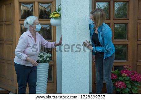 Senior woman with face mask in house quarantine talks to neighbor at safety distance Royalty-Free Stock Photo #1728399757
