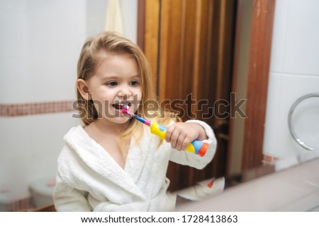 
little girl brushes her teeth with an electric toothbrush, reflection in the mirror, children's electric toothbrush Royalty-Free Stock Photo #1728413863