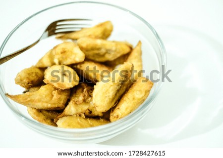 Delicious eating fried bananas served in a transparent glass bowl with a fork placed on a white table.