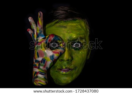 Photo of a man's face in a dark key on a black background. Face and hand are painted with colored paints. Creative photo of a man in minimalistic black. Royalty-Free Stock Photo #1728437080