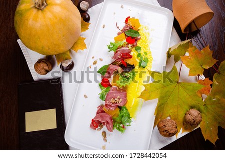 Pumpkin and gravy salad with Spanish jamon, pepper, herbs on a white plate decorated with seeds