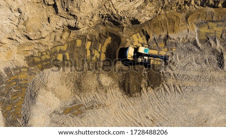 Aerial view, orange excavator with truck working in quarries site. Construction digger machine. Heavy equipment for digging in the ground. Top view from drone.
