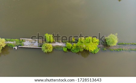 Aerial view of beautiful countryside at sunset. Summer rural landscape with old bridge, dirt road, green trees, hills, people in boat on the river. Top view of country road, forest, blue water. Nature