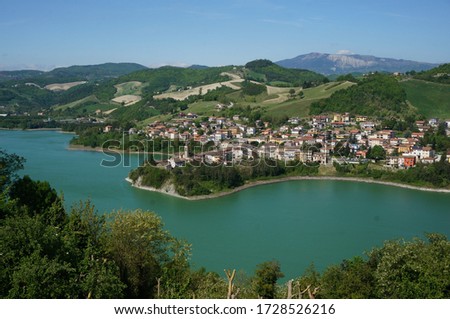 High angel view of lake and old town with young green plants surrounded by mountains, blue and clear sky in summer, Sassocorvaro, The Marche, Italy