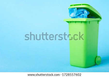 green trash can with polyethylene waste on a blue background with place for text