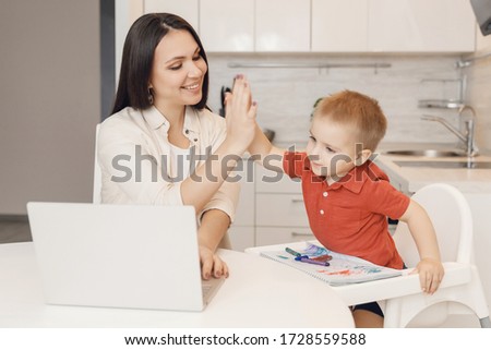 Mom with her son rejoices success of table in kitchen with laptop makes gesture to give five with palm. Concept training, spending time together.