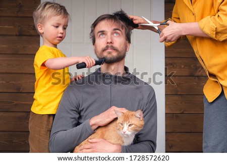Family haircut at home during quarantine lockdown, domestic hairdressers. Mother cutting hair to father and little child boy cut dad beard with clipper. Beauty and selfcare at home lifestyle. Royalty-Free Stock Photo #1728572620