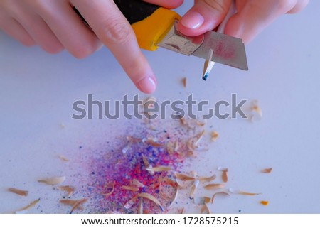 Woman painter artist sharpening blue pencil using sharp knife, hands closeup. Teacher sharpen blue pencil for her students on white table. Preparing to work in art studio.