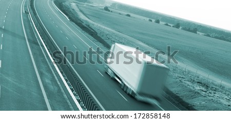 Red truck on blurry asphalt road over blue cloudy sky background 
