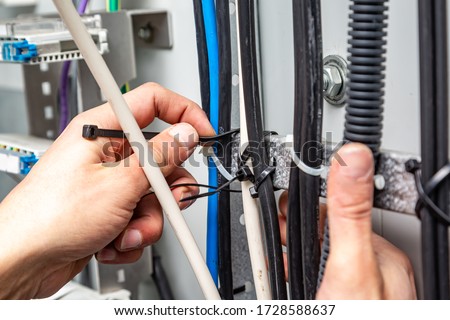 Hands fasten the cable ties on the cable, which are on the cable tray. Close-up. Horizontal orientation. Royalty-Free Stock Photo #1728588637