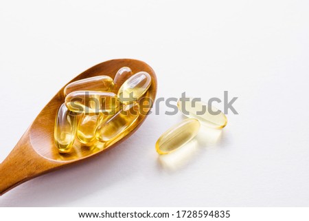 Fish fat oil capsules Omega-3  in wooden spoon on white background, close up