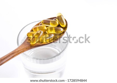 Fish fat oil capsules Omega-3  in wooden spoon and a glass of water on white background, close up