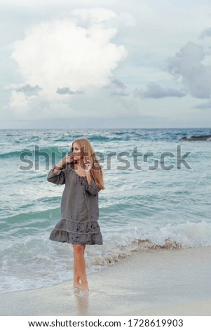Evening photo shoot for a beautiful blonde girl with long hair in a gray dress. Walking along the beach at sunset. Vacation and Travel Concept. 