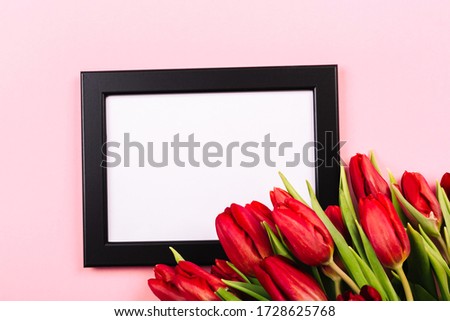 Black photo frame as a template with a bouquet of red tulips on a pink background. Beautiful festive vertical blank for congratulation text or certificate. A place for a memorable photo.