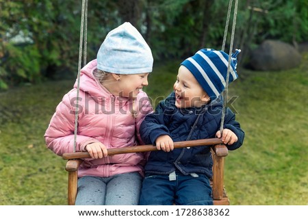 Two cute adorable playful caucasian siblings boy girl child enjoy having fun swinging wooden swing at backyard together with father. Little toddler brother and sister laughing at playing outdoors. Royalty-Free Stock Photo #1728638362