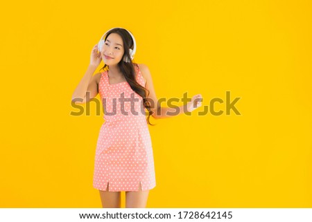 Portrait beautiful young asian woman listen music with smart mobile phone and headphone on yellow isolated background