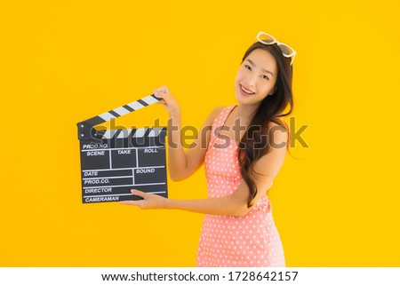 Portrait beautiful young asian woman with clapper board for cinema movie on yellow isolated background