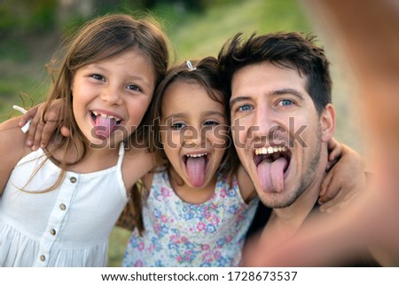 Authentic shot of happy carefree young brother and his little sisters are having fun to make a selfie or video call to parents or relatives on a green nature background in a sunny day.