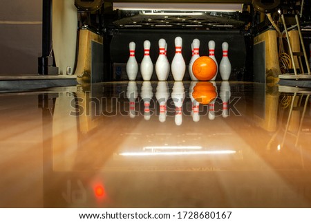 White bowling pins and an orange ball on a bowling alley. Beautiful reflection. Close-up. Front view.