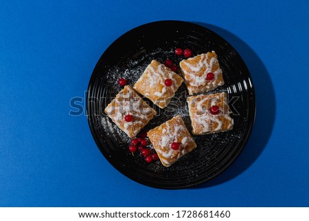 gourmet French pastries decorated with red currant berries in a black plate on a blue background. mouth-watering dessert.