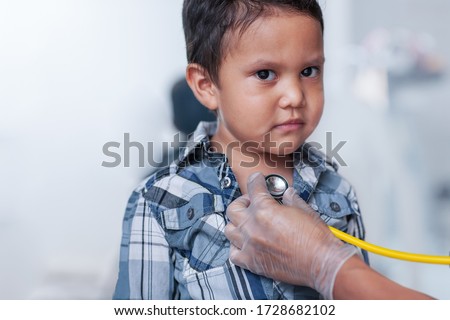 A preschool age boy getting a heart screening, using a stethoscope on chest with a buttoned down shirt.