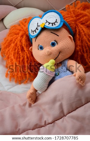 Handmade doll with orange hair sleeping on bed.