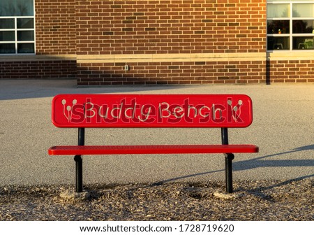 New outdoor buddy red bench for parents while waiting for kids at a public school playground. Friendship seat, concept idea of smile and happy furniture for kids or people when sitting together. Royalty-Free Stock Photo #1728719620