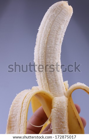 yellow peeled banana in hand on gray background
