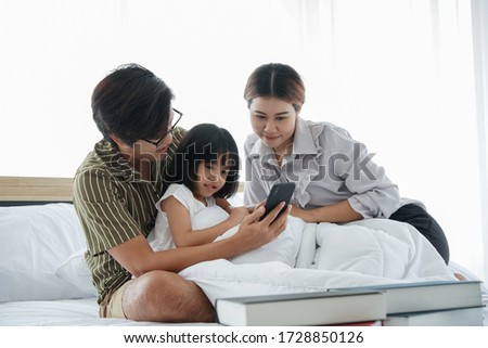 Family selfie with dad mom little daughter. Self portrait of happy young Asian father mother and their little girl taking selfie while sitting under blanket on the bed in bedroom