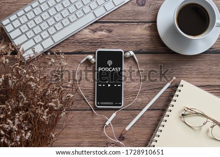 podcast audio content concept. podcast application on mobile smartphone screen on wooden table with coffee cup, earphones, glasses, notebook and pencil. broadcast media