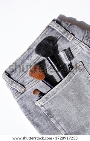 Large makeup brushes in pocket of gray jeans. Concept, commercial work of a makeup artist, for printing business cards and brochures on white background