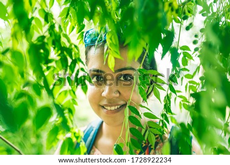 A young Indian girl looking through green leaves of a Neem tree in a park on a beautiful morning. People spending time in nature.