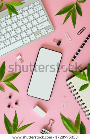 Feminine workspace vertical mockup. Empty phone screen, office stationery, silver keyboard and leaves on a pink desk with copy space for app or mobile site screenshot