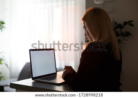 Unrecognizable woman working on her computer from her home office facing the spectacular metropolitan city at sunrise. Businesswoman doing research from a luxury hotel room