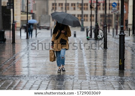 A girl with a black umbrella and a paper bag walks down the street in the rain Royalty-Free Stock Photo #1729003069