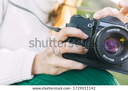 Portrait of a beautiful girl in the park with a camera in her hands. He takes pictures on a film camera, laughs, enjoys life at sunset.
