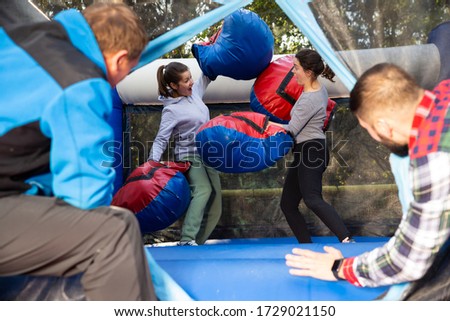 Two cheerful women having funny battle by big boxing gloves on inflatable arena at amusement park