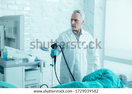 Serious mature doctor holding a modern endoscope and preparing for the procedure Royalty-Free Stock Photo #1729039582
