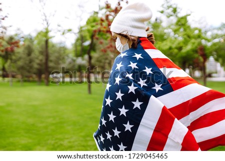 Young girl in a protective mask with the flag of America. Independence Day of America. 4th of July. Coronavirus in America. The concept of preventing the spread of the epidemic. 