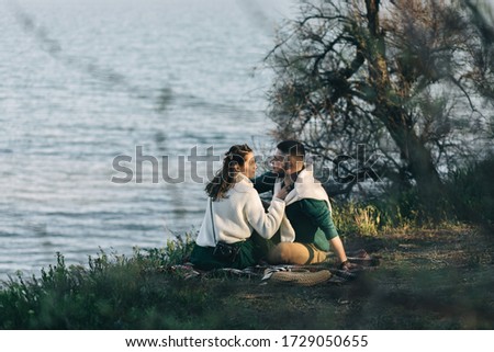 

A guy and a girl love each other, smile, hug, kiss, laugh, enjoy life in the forest on the beach. A girl takes a picture of a guy's camera on a cliff, sunset on the background.
